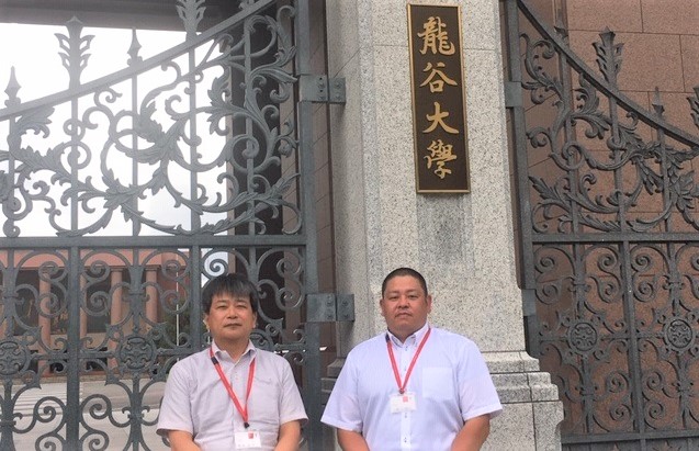 龍谷大学を背景にして、職員2名が撮影された写真